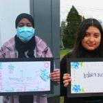 Several students stand holding hand drawn signs that say Welcome in different langauges